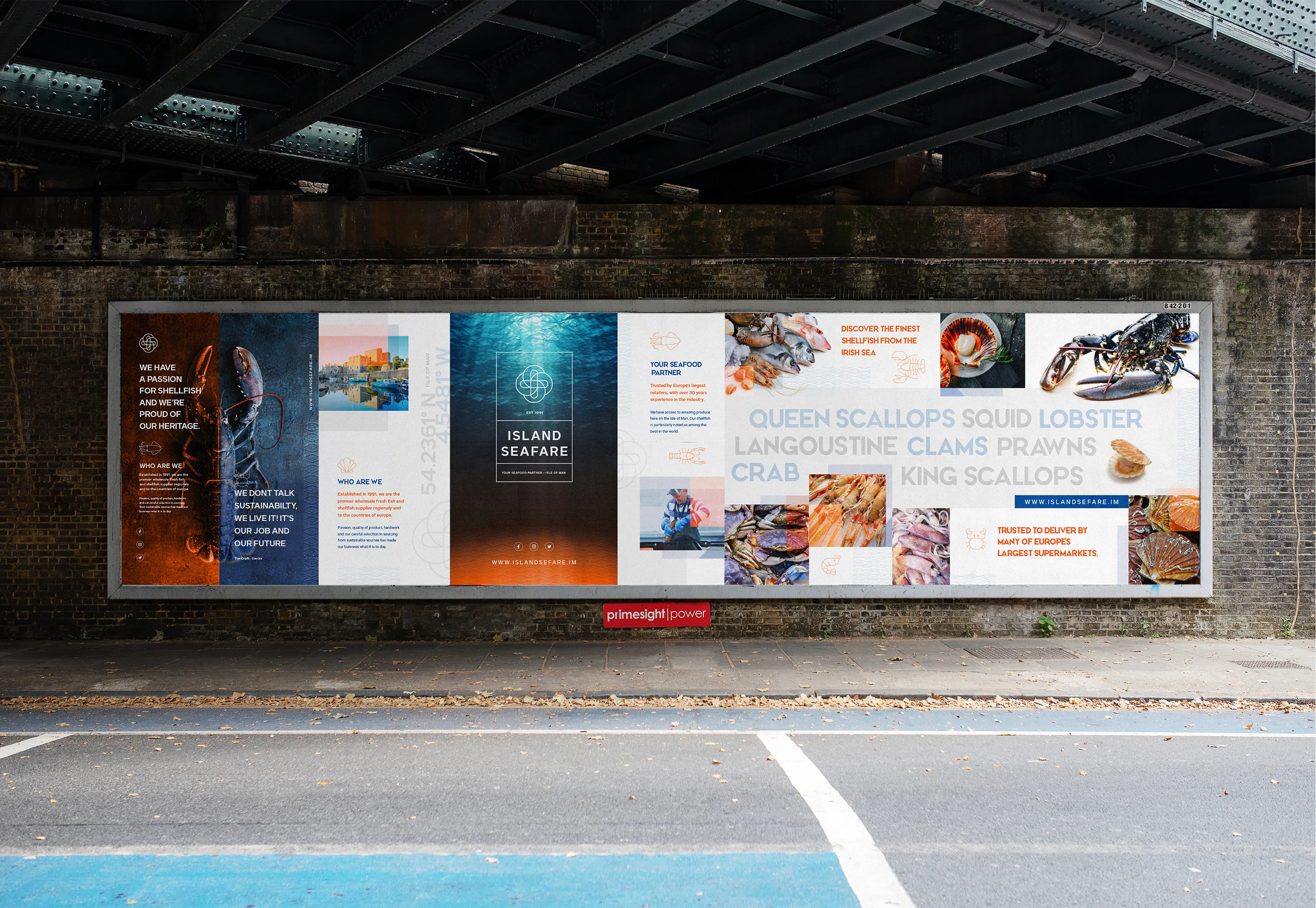 Large format outdoor billboard displayed on a brick wall beneath a railway bridge showing the Island Seafare brand campaign featuring lobster and shellfish photography, the Island Seafare logo, product list including Queen Scallops, Squid, Lobster, Langoustine, Clams, Prawns, Crab and King Scallops, and the tagline Trusted to Deliver by Many of Europe's Largest Supermarkets, with website URL www.islandsefare.im